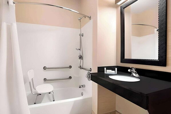 A modern bathroom with a white bathtub, a white chair, a black sink, and a large mirror.