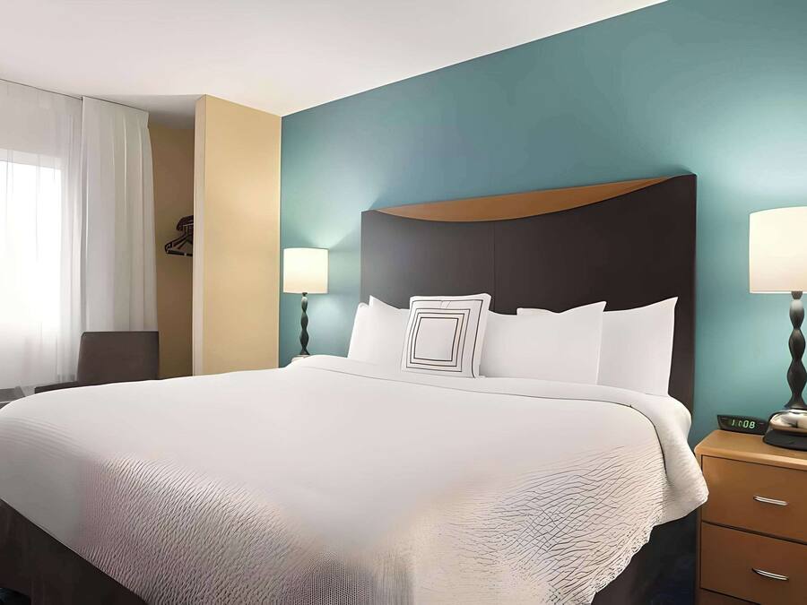 Una habitación de hotel con una cama grande, dos lámparas de noche, una mesita de noche y una ventana con cortinas.