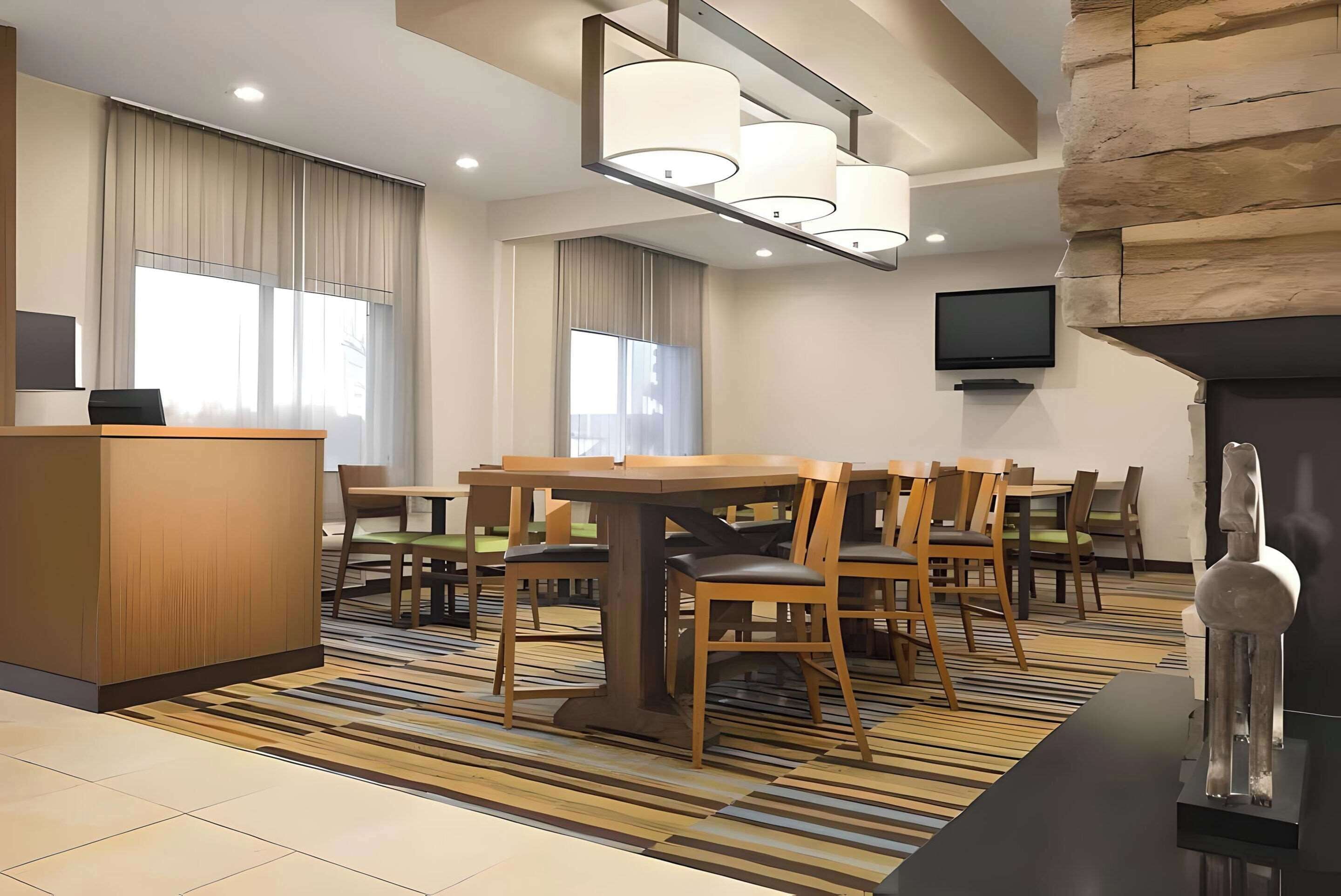 Un hall d’hôtel comprenant un comptoir de réception, un espace repas avec des tables et des chaises, un téléviseur à écran plat fixé au mur et un mur décoratif en pierre.