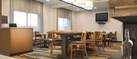 Un hall d’hôtel comprenant un comptoir de réception, un espace repas avec des tables et des chaises, un téléviseur à écran plat fixé au mur et un mur décoratif en pierre.