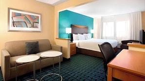 A hotel room with a bed, a sofa, two small tables, a desk, a TV, and a painting on the wall. - Dubuque Inn & Suites (Dubuque)