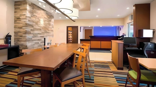 A modern hotel room with a wooden dining table, chairs, a stone accent wall, a kitchen area, and a television. - Dubuque Inn & Suites (Dubuque)