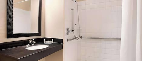 A bathroom with a black countertop sink, a large mirror, and a shower with a grab bar.