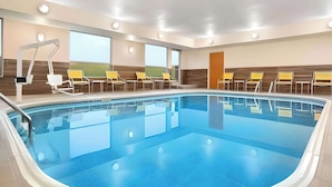 An indoor swimming pool with clear blue water, surrounded by yellow and white lounge chairs, and a sunbed. - Dubuque Inn & Suites (Dubuque)