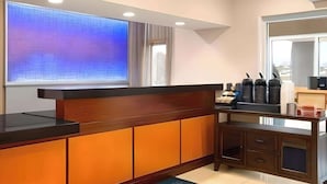 A modern reception desk with a wooden finish and a black countertop. There is a large window with a blue-tinted glass feature, and a mirror above the desk. - Dubuque Inn & Suites (Dubuque)