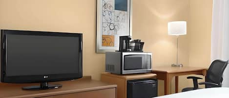 A hotel room with a television, a microwave, a coffee maker, a desk, and a chair.