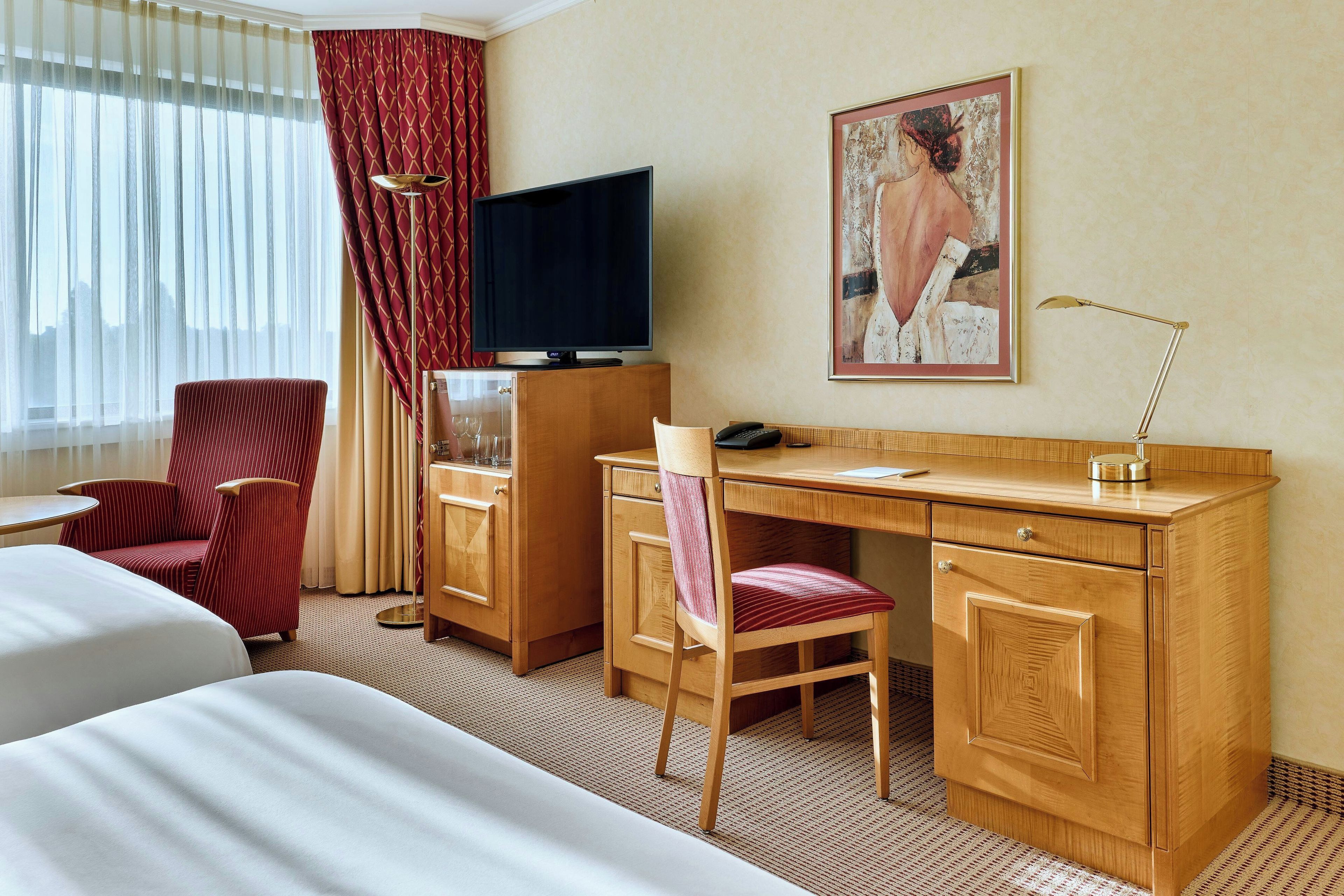 Ein Hotelzimmer mit Bett, Schreibtisch, Stuhl, Fernseher und einem Bild an der Wand.