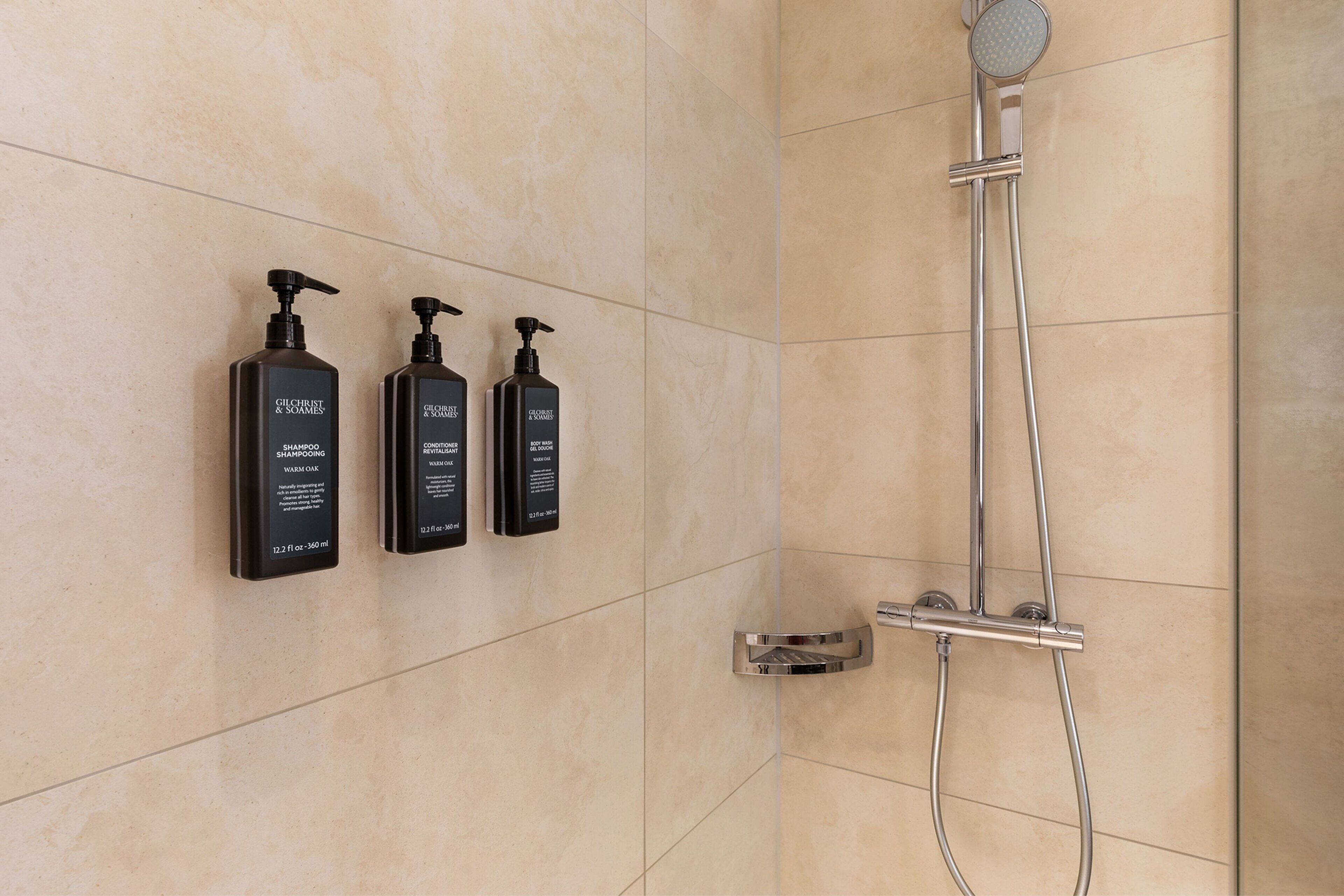 Een badkamer met drie zwarte shampoo flessen aan de muur en een chromen douchekop.