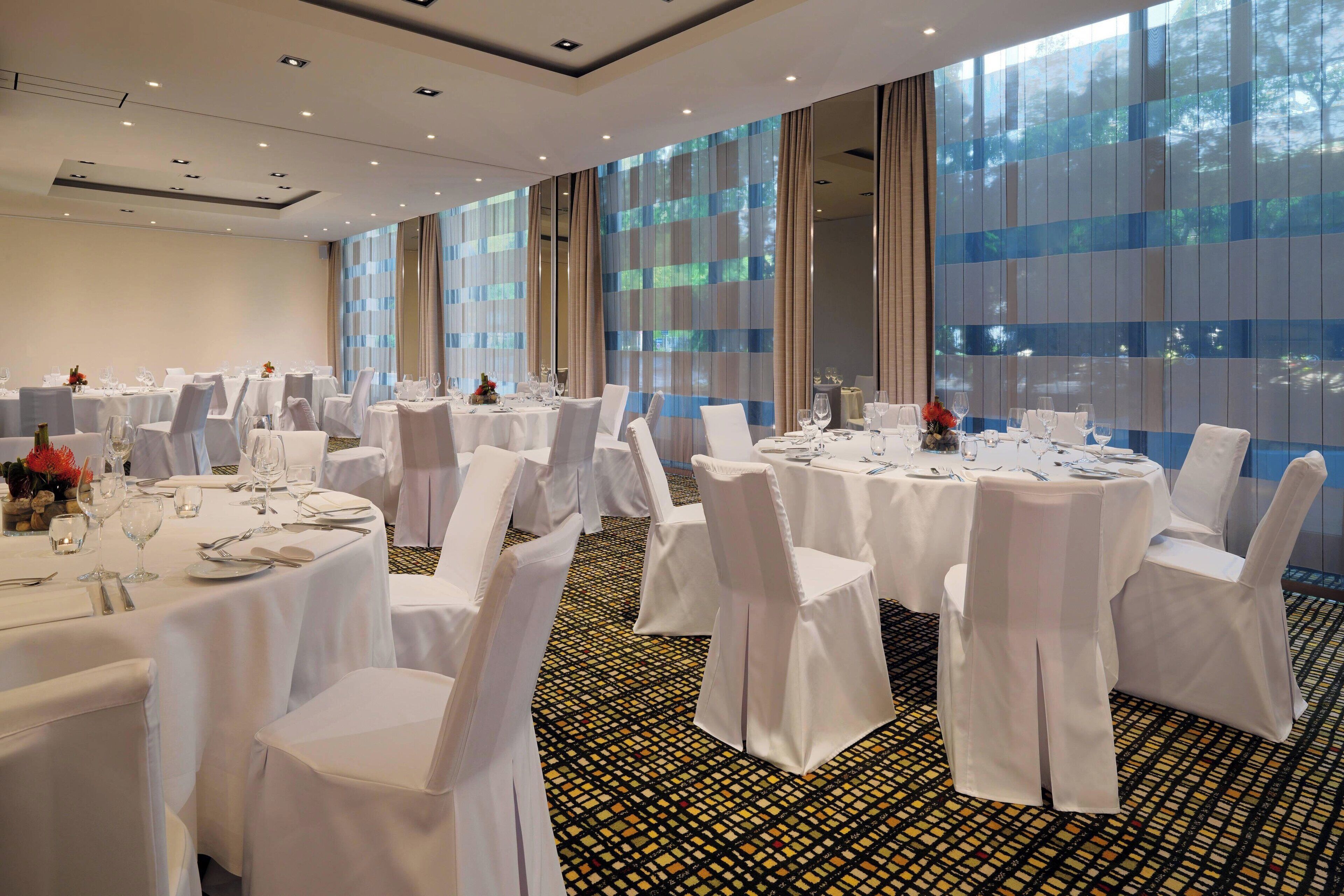 A banquet hall with round tables, white chairs, and large windows.