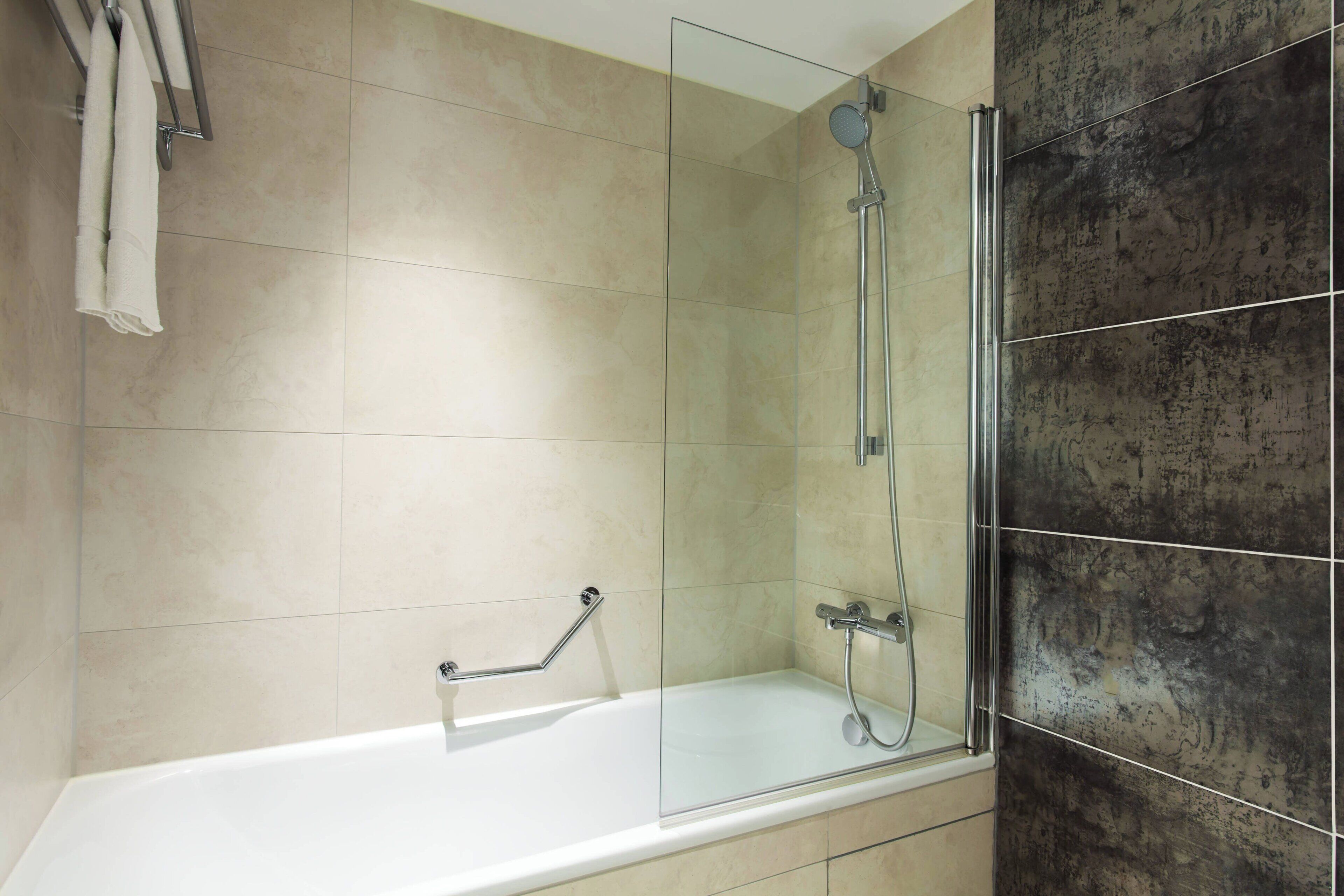 A modern bathroom with a glass-enclosed shower, a white bathtub, and a towel rack.