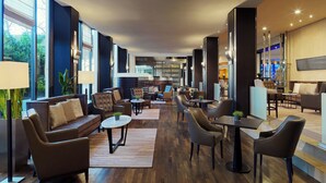 A spacious lobby with leather seating, a coffee table, and a large window providing a view of the outdoors. - Sheraton Essen Hotel (Essen)