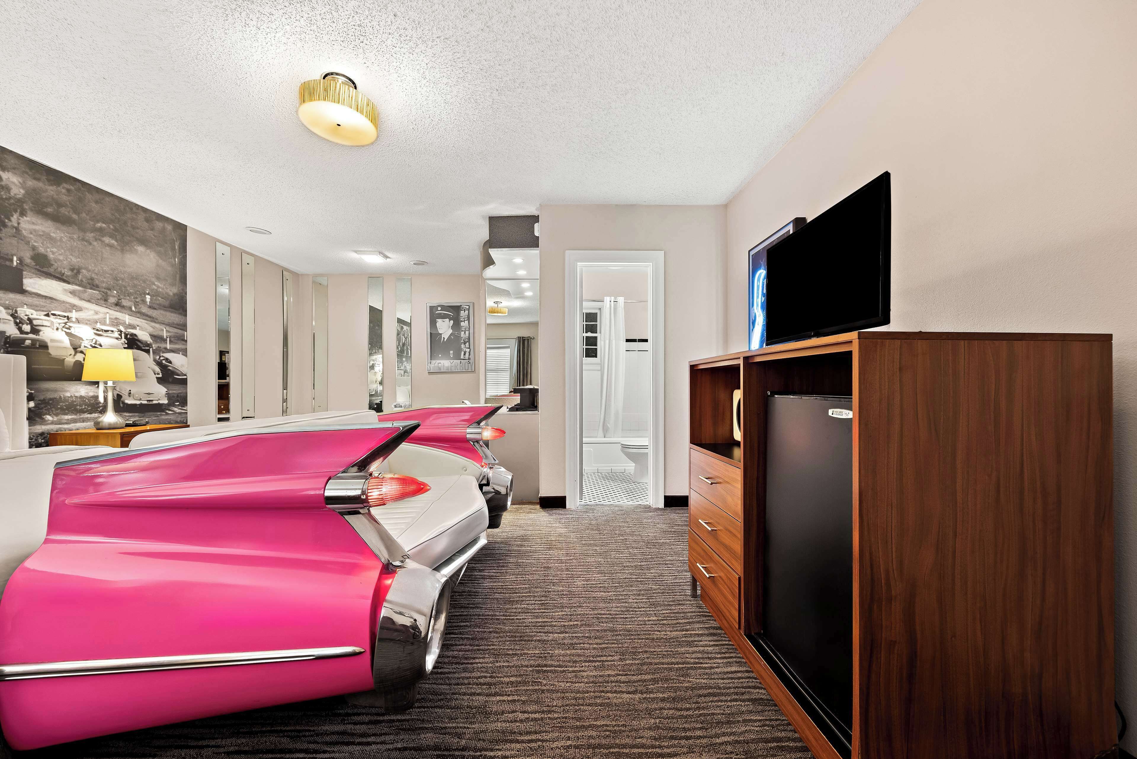A hotel room with a large bed, a television, a refrigerator, and a carpeted floor.