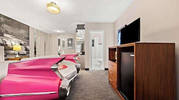 A hotel room with a large bed, a television, a refrigerator, and a carpeted floor.