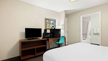 A hotel room with a bed, a desk with a TV, a chair, a microwave, and a painting on the wall.