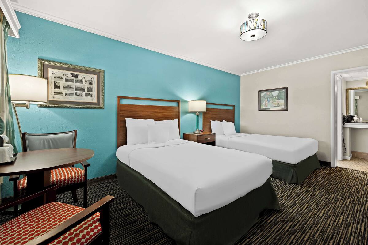 A hotel room with two beds, a desk, a chair, and a lamp.