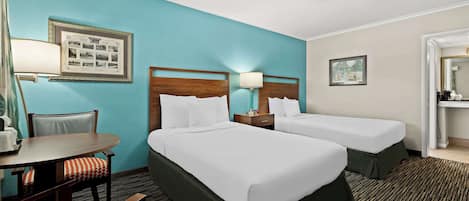 A hotel room with two beds, a desk, a chair, and a lamp.