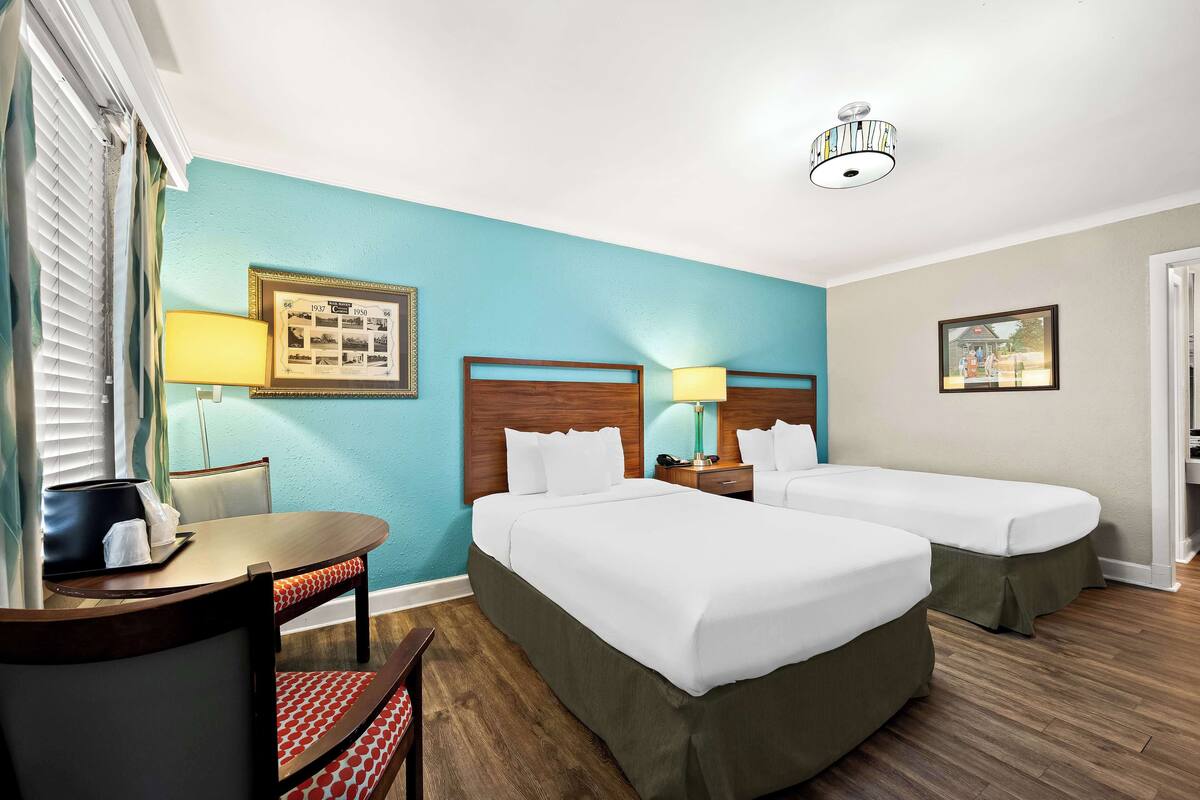 A hotel room with two beds, a dining table, and a chair.