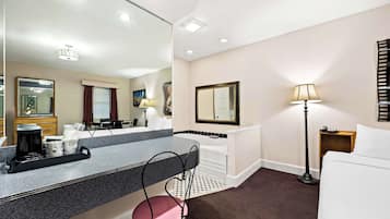 A hotel room with a large mirror, a bed, a bedside table with a lamp, a chair, and a coffee maker on the counter.