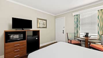 Habitación de hotel con cama, televisión, minibar, escritorio con silla y ventana con cortinas.