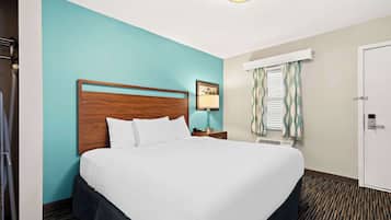 Quarto de hotel com uma cama grande, uma mesa de cabeceira com abajur, uma janela com cortinas e uma porta.