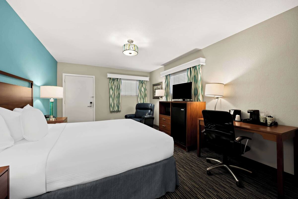 A hotel room with a large bed, a desk with a computer, a chair, a TV, and a lamp.