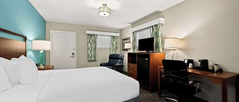 Une chambre d’hôtel avec un grand lit, un bureau avec un ordinateur, une chaise, une télévision et une lampe.