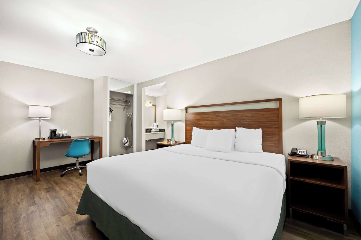 A hotel room with a large bed, a desk with a chair, a nightstand, and a mirror.