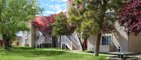 A residential building with a red roof, a staircase leading to the entrance, and a picnic table in the yard.