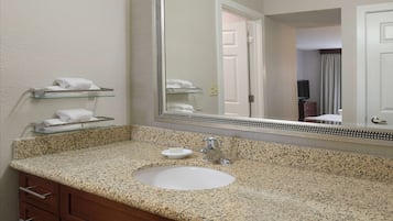 A bathroom with a granite countertop sink, a large mirror, and a wooden vanity with drawers.