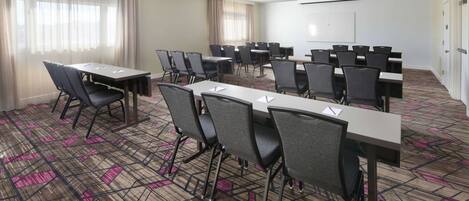 A conference room with multiple tables and chairs, a whiteboard, and a patterned carpet.