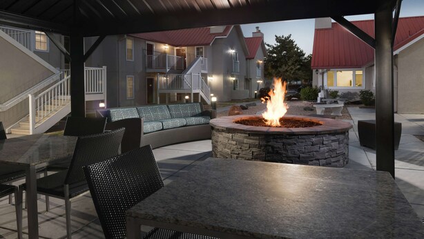 An outdoor patio area with a stone fire pit, seating, and a covered walkway.