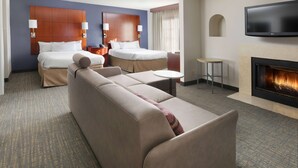 A hotel room with a large bed, a sofa, a small table, a TV, and a fireplace.