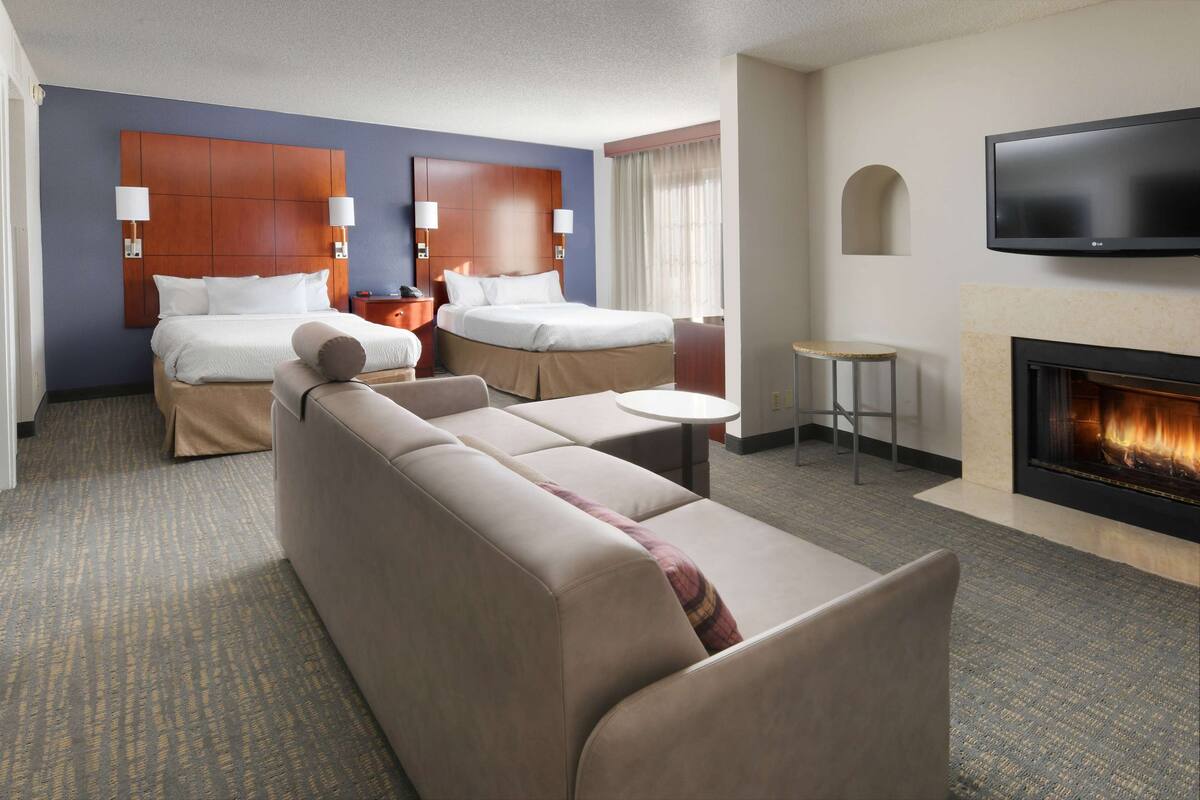 Una habitación de hotel con una cama grande, un sofá, una mesita, un televisor y una chimenea.