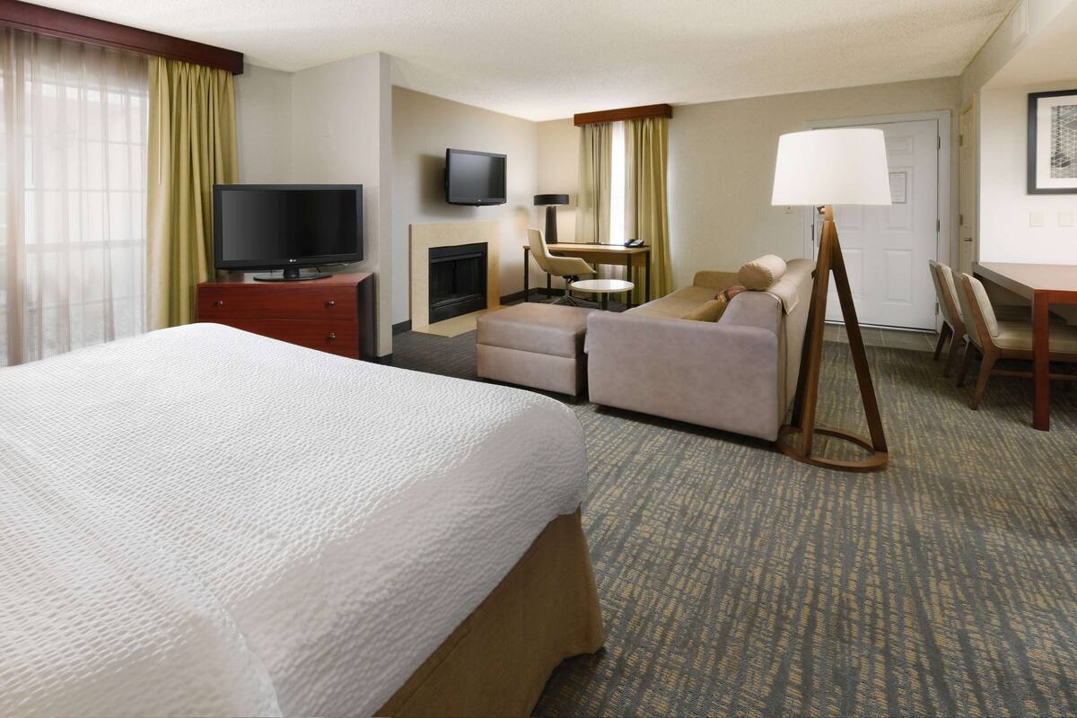 Habitación de hotel con cama, televisión, escritorio con silla, sofá y lámpara.