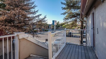 Una terraza de madera con baranda blanca, que da vista a un estacionamiento y un edificio con el letrero 'Sonesta ES'.