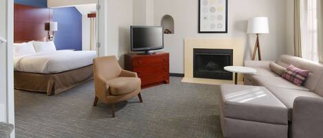 A hotel room with a bed, a TV on a wooden stand, a sofa, a chair, and a fireplace.