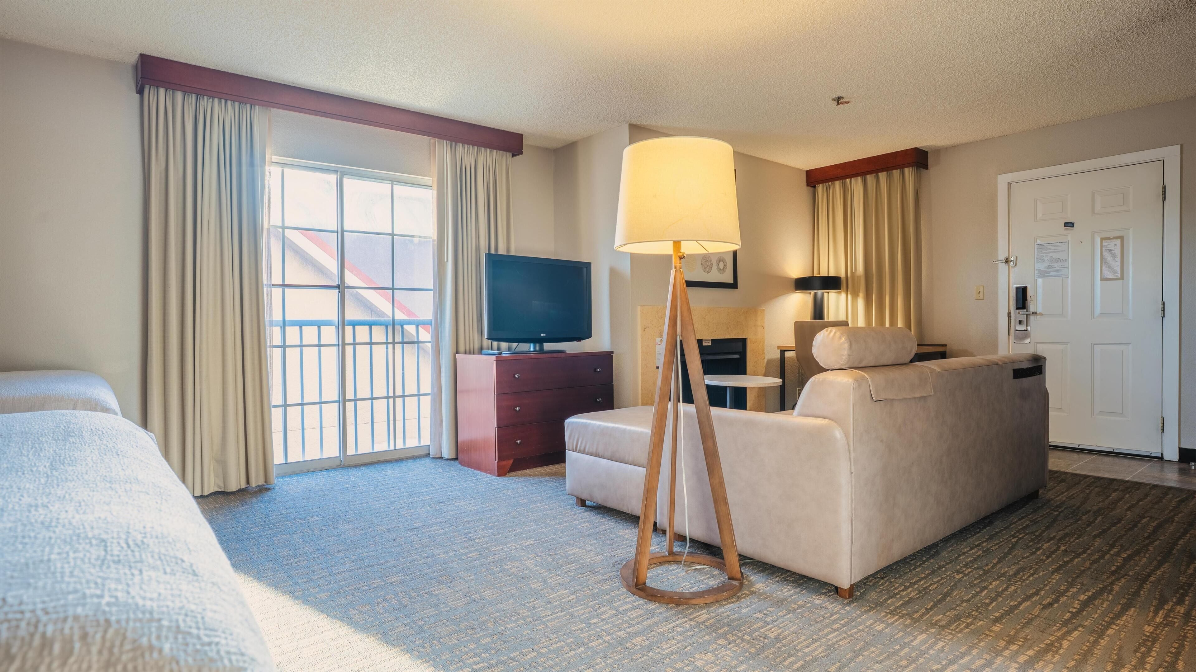 A hotel room with a bed, a sofa, a TV, a lamp, and a desk.