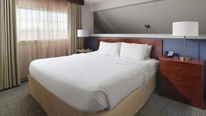A hotel room with a large bed, a nightstand with a lamp, a phone, and a window with curtains.
