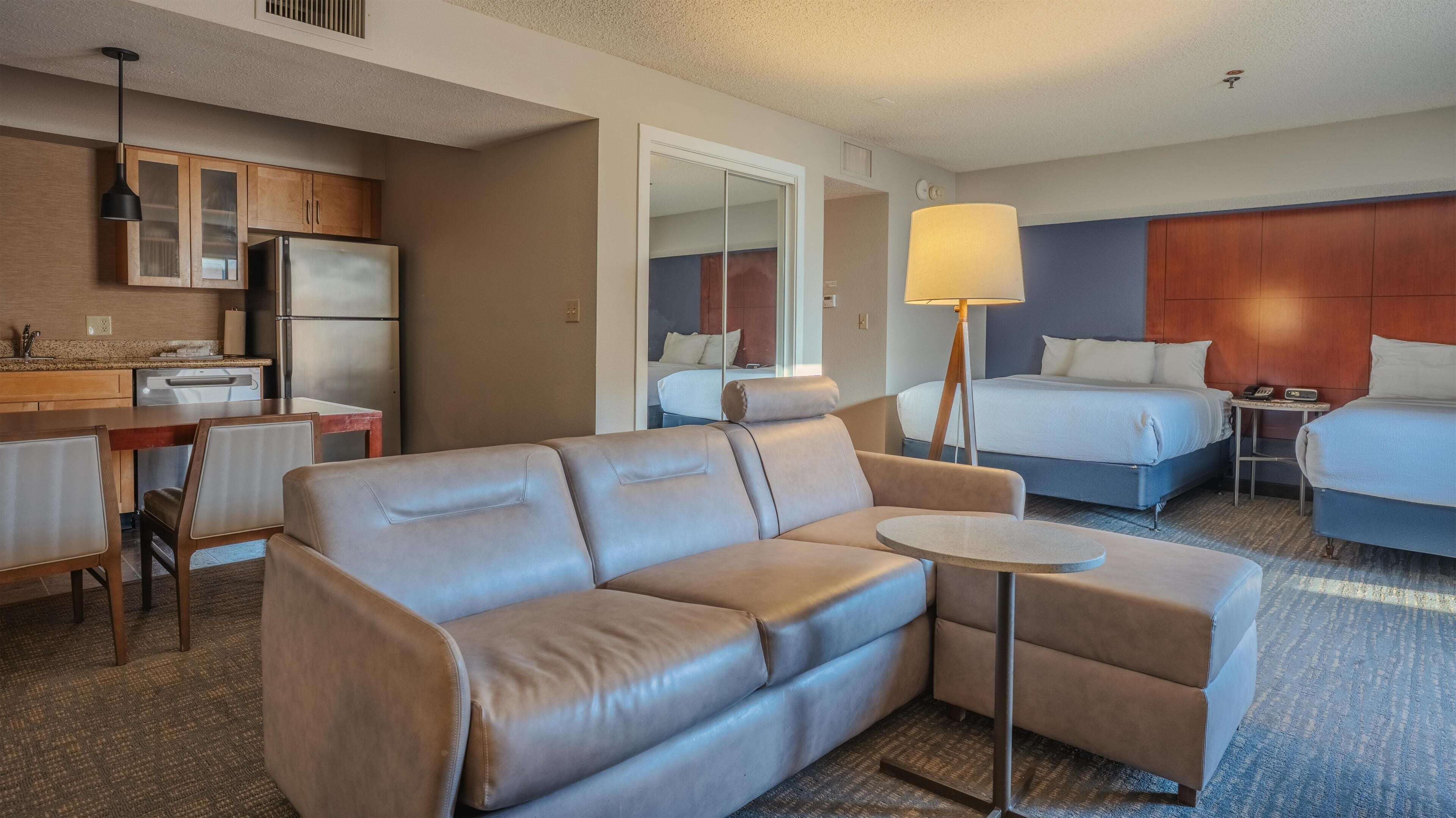 Ein Hotelzimmer mit einer Couch, einem kleinen Tisch, einem Bett, einem Schreibtisch und einer Küchenzeile.