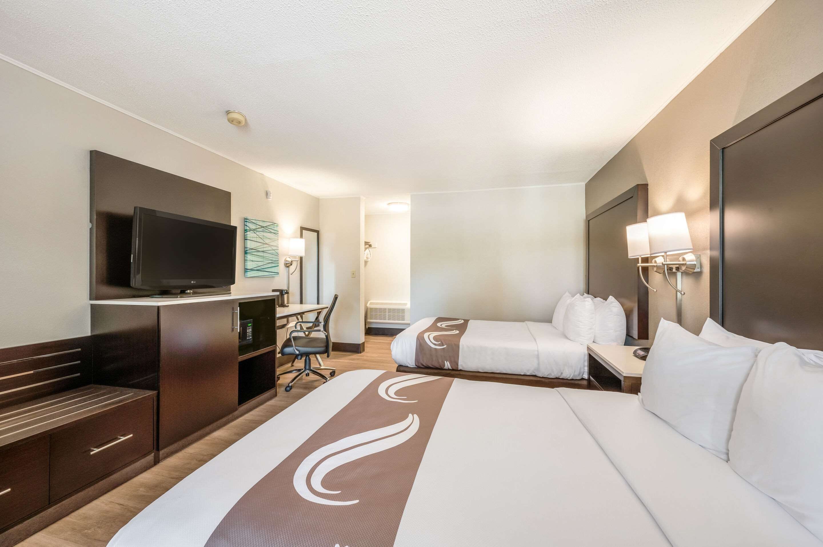A hotel room with a large bed, a desk with a chair, a television, and a bathroom with a shower.