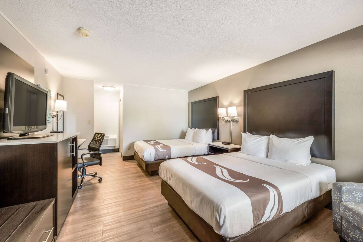A hotel room with two beds, a desk with a television, a chair, and a large mirror.