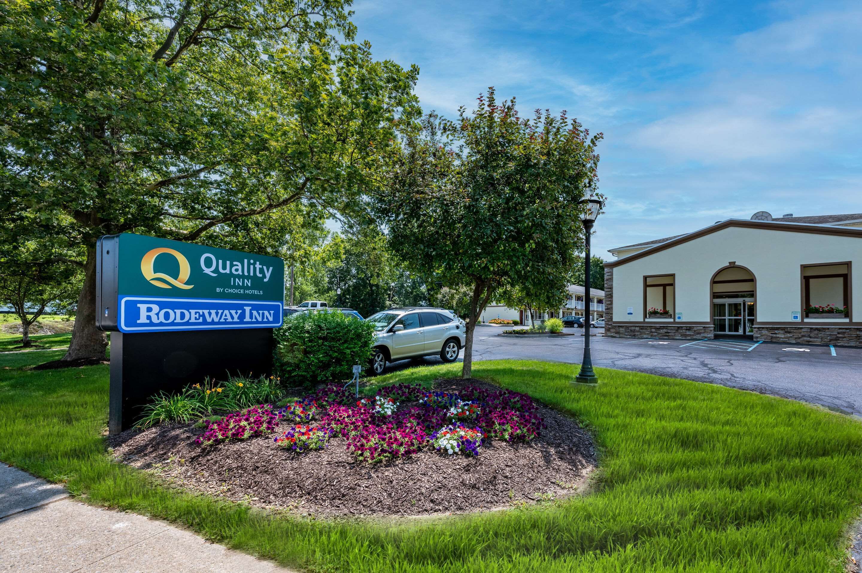 Letrero de Quality Inn by Choice Hotels con un parterre floral frente al hotel.