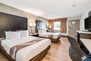 A hotel room with two beds, a desk, a chair, a television, and a window with curtains.