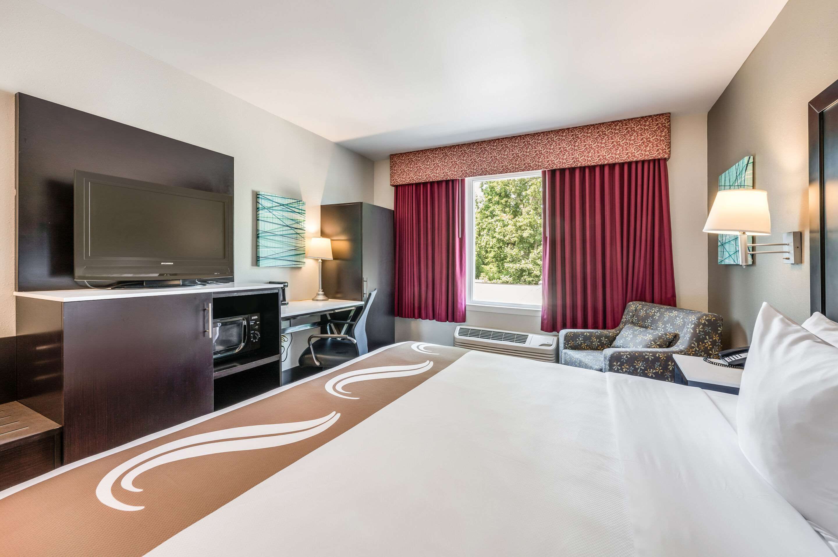 A hotel room with a large bed, a desk with a flat-screen TV, a chair, and a sofa.