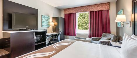 A hotel room with a large bed, a desk with a flat-screen TV, a chair, and a sofa.
