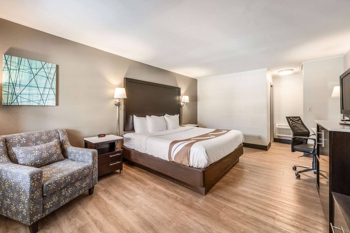 A hotel room with a bed, a desk, a chair, and a TV.