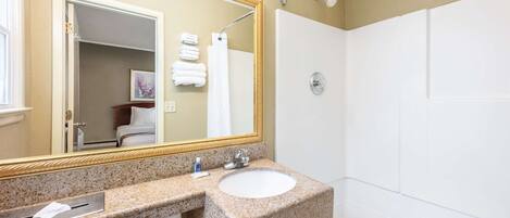 Baño con lavamanos de encimera de granito, un espejo grande y zona de ducha.