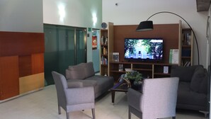 A modern waiting area with a sofa, chairs, a coffee table, a television, and a bookshelf.