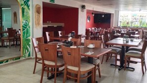 A spacious restaurant with multiple dining tables and chairs, a large mirror, and a tropical-themed wall design.