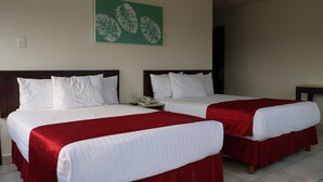 Two single beds with white linens and red bedspreads, a green leaf artwork on the wall, and a small bedside table with a phone.